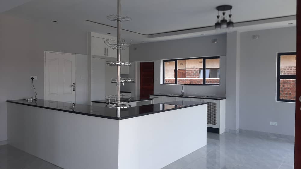 Open kitchen with a black stone island, white base units and a suspended utensil rack