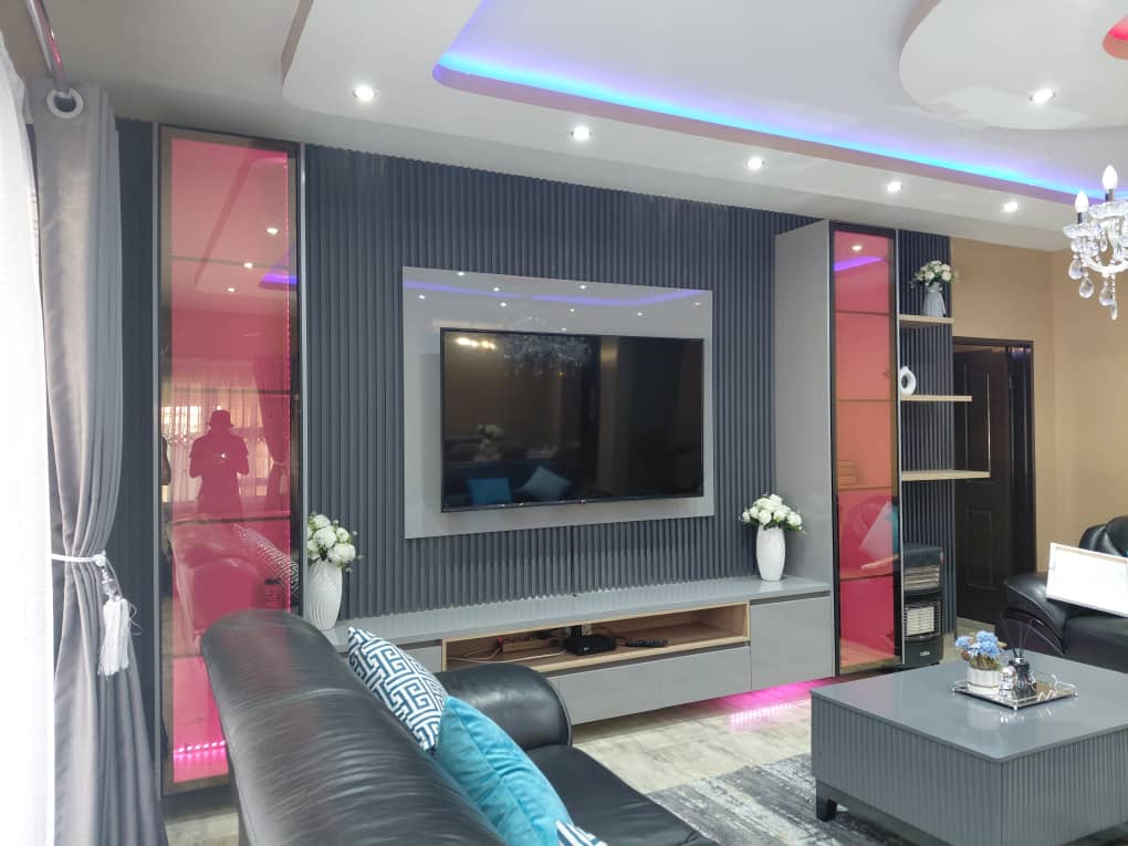 Living room TV wall with fluted panelling, pink-tinted glass towers and a blue-lit tray ceiling