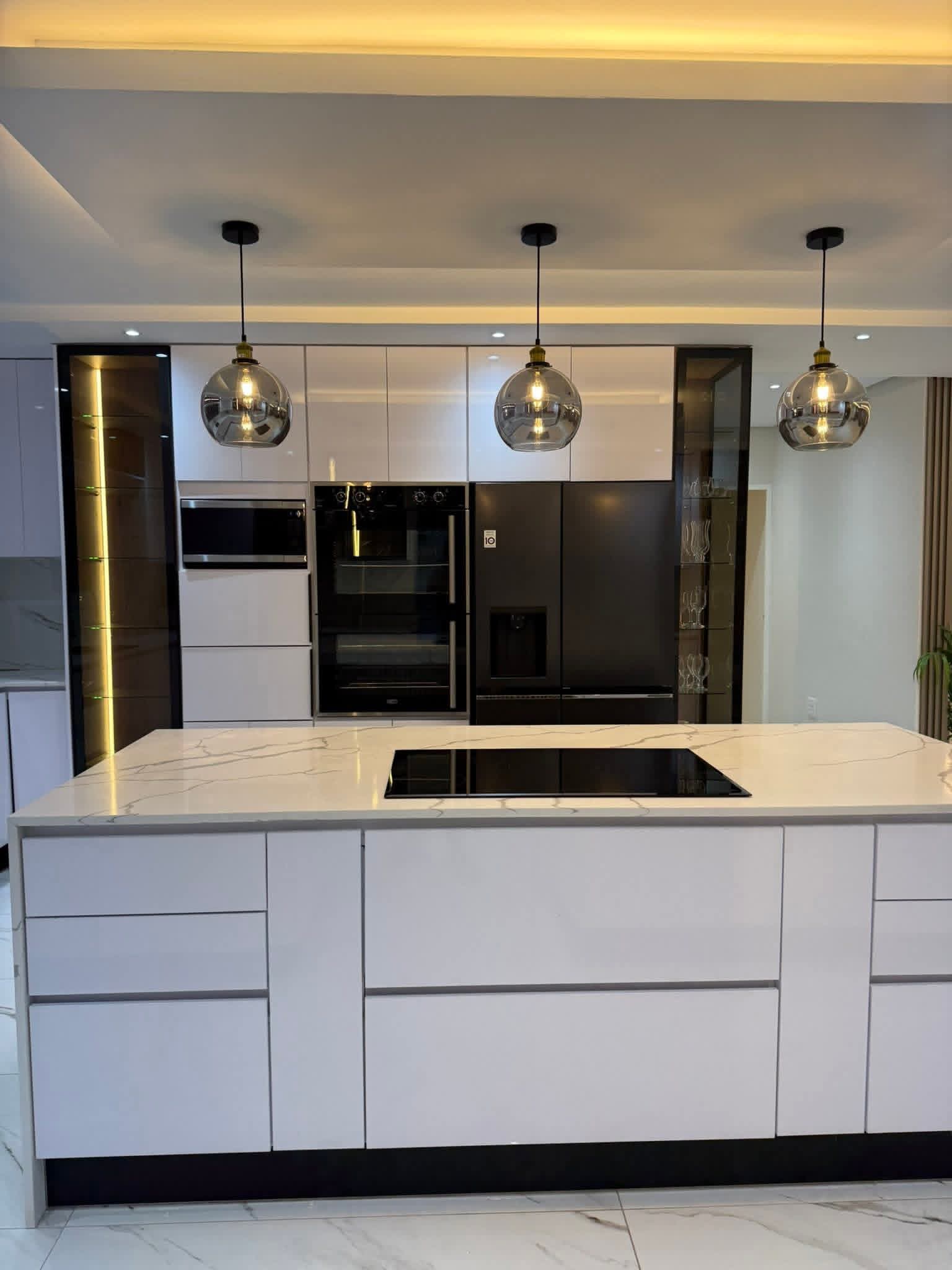 Front view of a marble kitchen island with three smoked-glass pendants and integrated cooktop